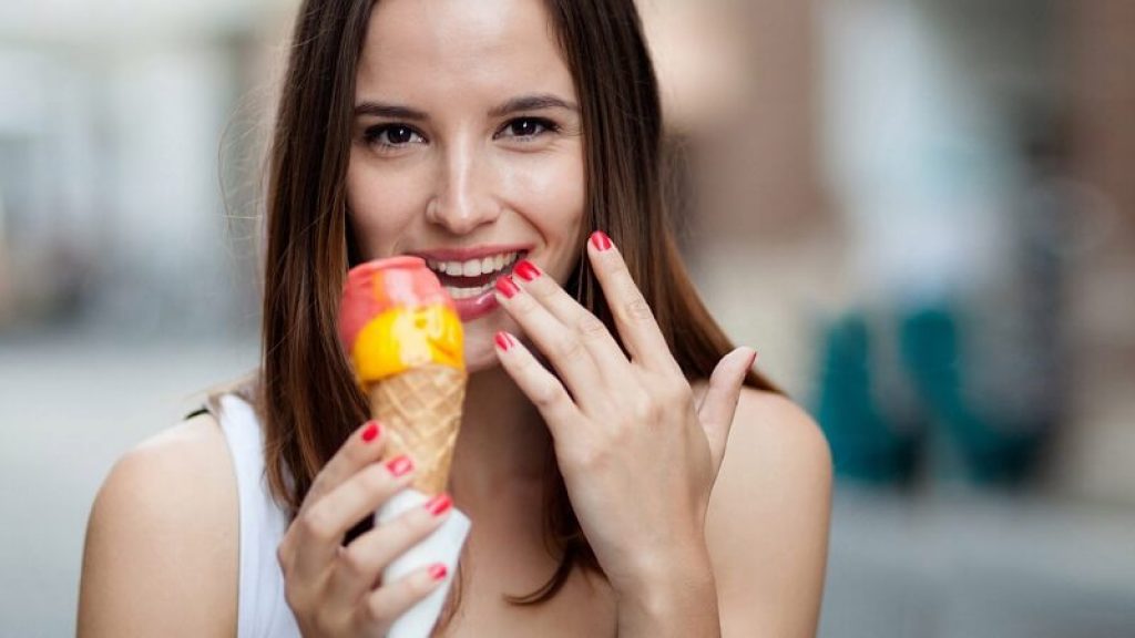 Kvinna äter gul och röd glass